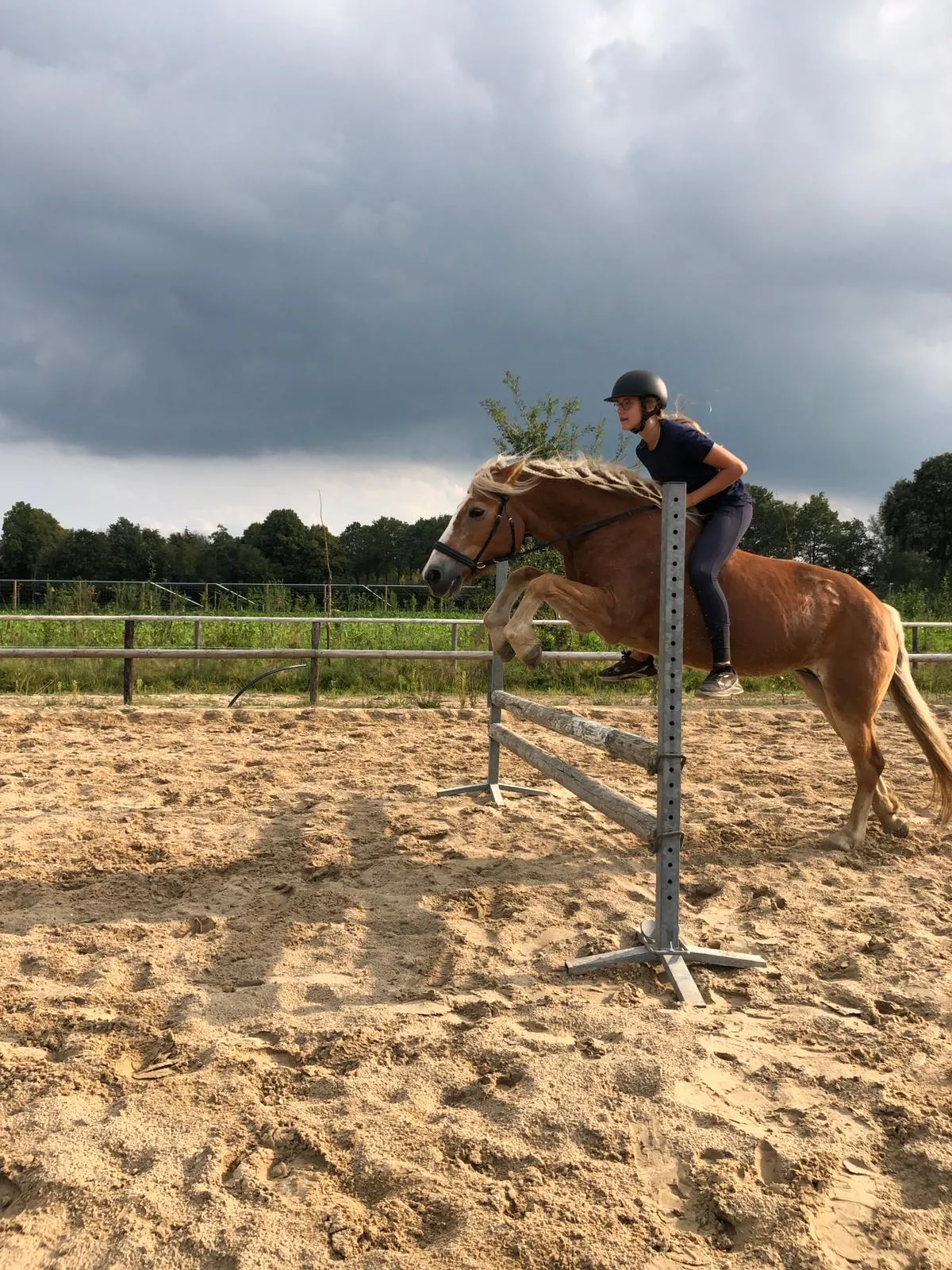Lease baasje springt met haar pony over een balk in de buitenbak.